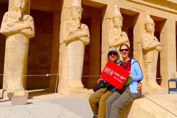 Happy travelers posing at the Temple of Hatshepsut in Luxor, sitting in front of towering Osiride statues at Deir el-Bahari during a private guided tour with WOW Tours Egypt.