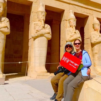 Happy travelers posing at the Temple of Hatshepsut in Luxor, sitting in front of towering Osiride statues at Deir el-Bahari during a private guided tour with WOW Tours Egypt.