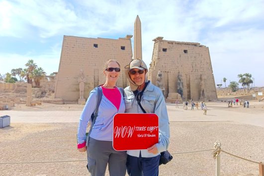 Couple standing before the massive First Pylon and obelisk at Luxor Temple under a bright Egyptian sky.