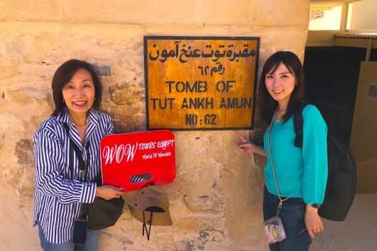 Two happy travelers at the entrance sign of the Tomb of Tutankhamun (KV62) in the Valley of the Kings, Luxor, during a guided Egyptology tour with WOW Tours Egypt // Luxor Front (8)