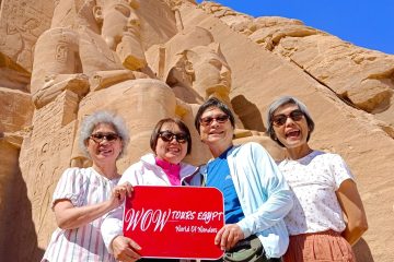 A joyful group of ladies visiting the Abu Simbel Temples in Aswan with WOW Tours Egypt, standing beneath the colossal statues of Ramses II on a private guided tour.