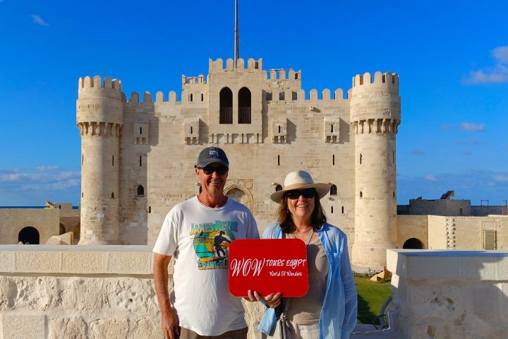 Two visitors holding a WOW Tours Egypt sign in front of the Citadel of Qaitbay in Alexandria, Egypt