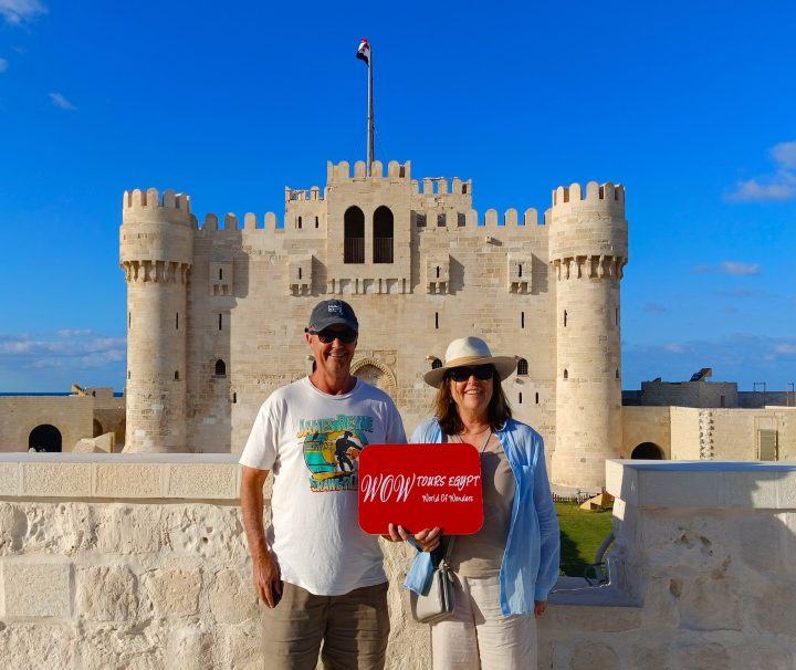 Two visitors holding a WOW Tours Egypt sign in front of the Citadel of Qaitbay in Alexandria, Egypt