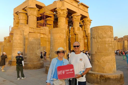 Happy couple standing at the Temple of Kom Ombo dedicated to Sobek holding the WOW Tours Egypt sign during a Nile Valley tour.