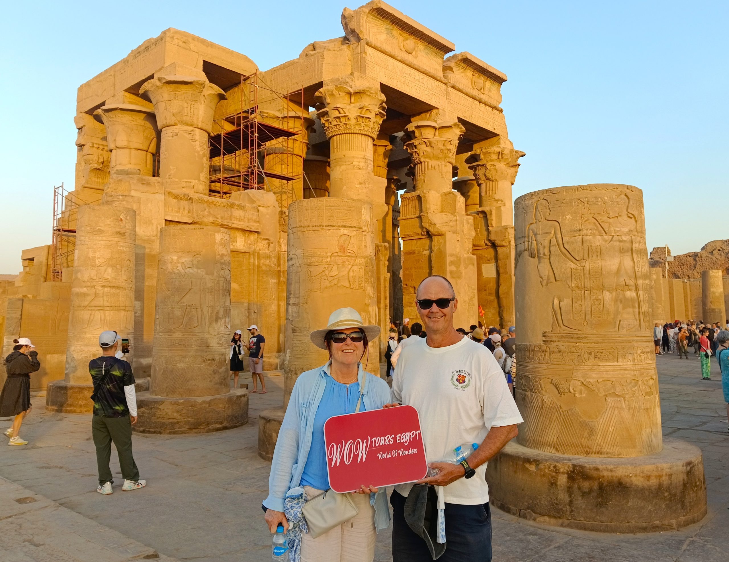 Happy couple standing at the Temple of Kom Ombo dedicated to Sobek holding the WOW Tours Egypt sign during a Nile Valley tour.