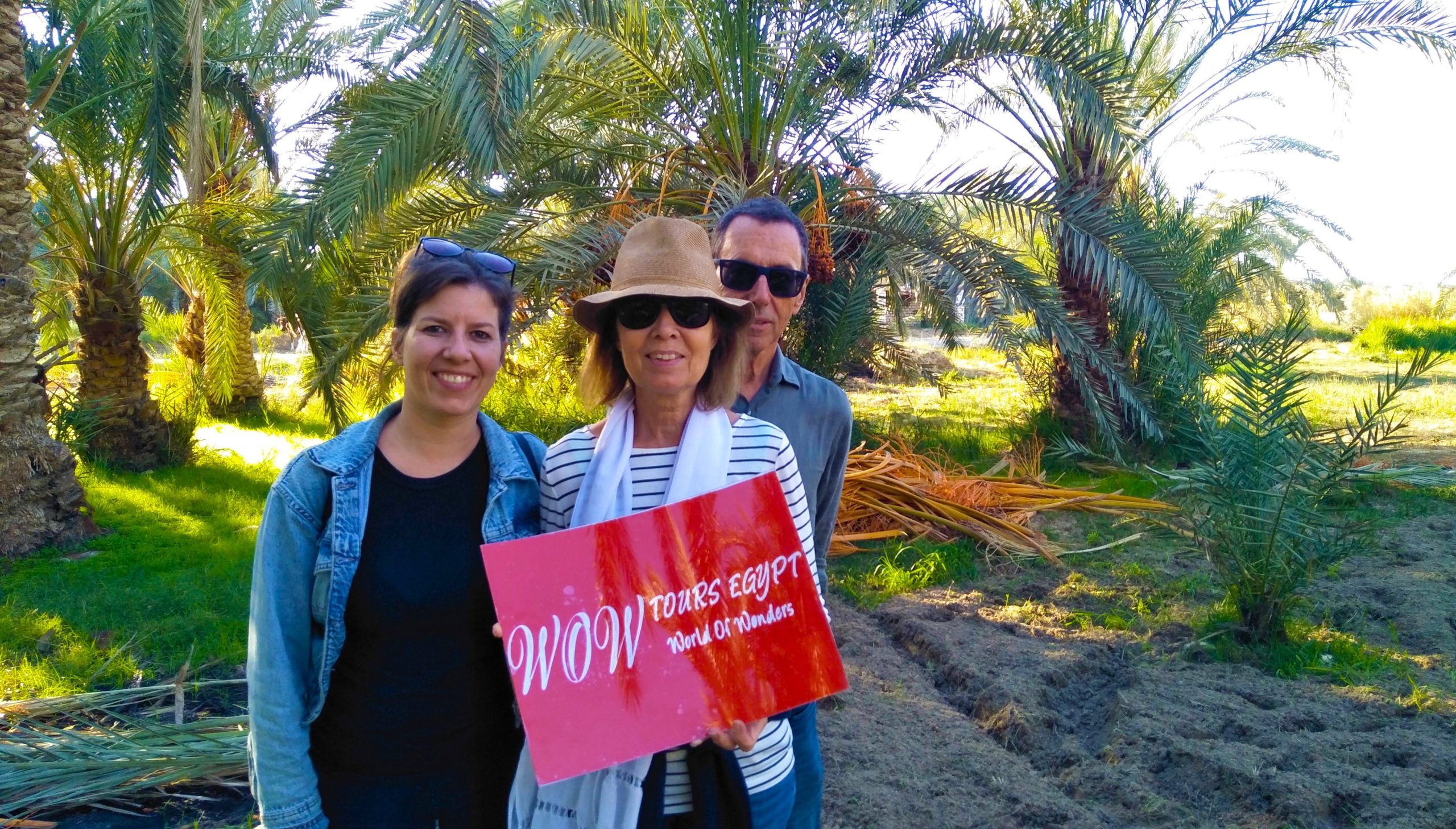 Travelers standing in a date palm farm in Rashid Egypt holding a WOW Tours Egypt sign during a local experience