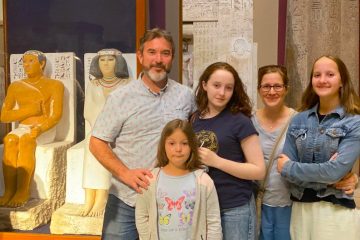 Family standing beside painted ancient Egyptian statues inside the Egyptian Museum in Cairo.