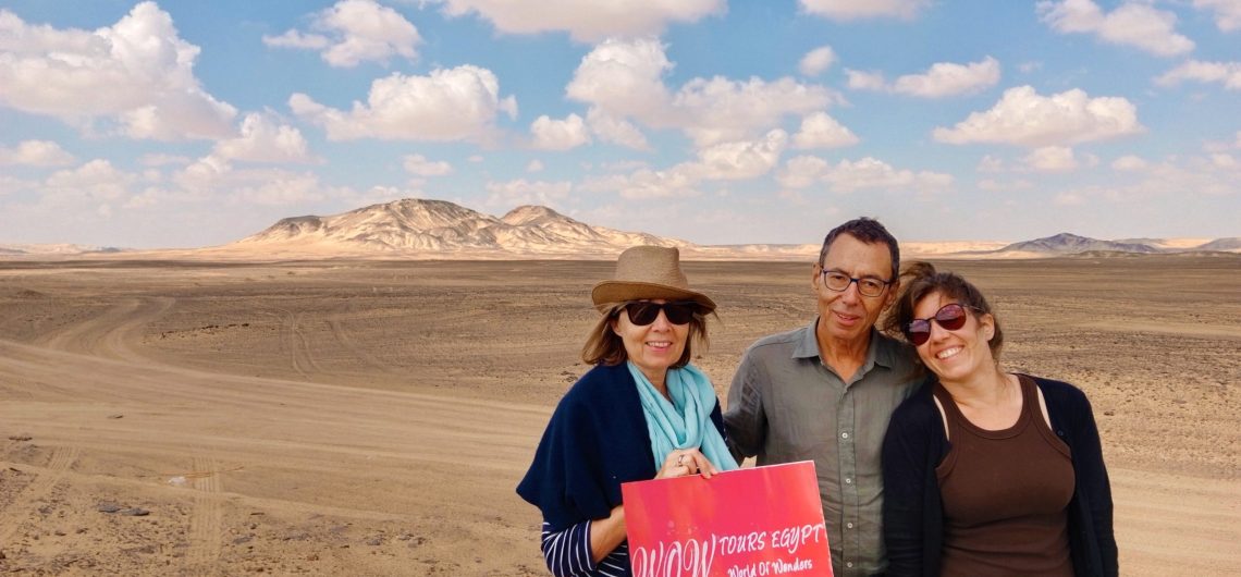 Three travelers surrounded by the vast Western Desert landscape and distant mountains near Kharga Oasis.