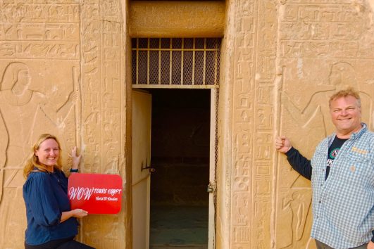 Couple standing at the entrance of the Tomb of Mereruka with hieroglyphs in Saqqara Egypt holding WOW TOURS EGYPT sign
