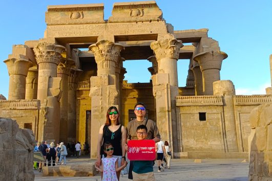 A happy family stands in front of the magnificent Temple of Kom Ombo in Upper Egypt, holding a WOW TOURS EGYPT // Luxor Front (9)