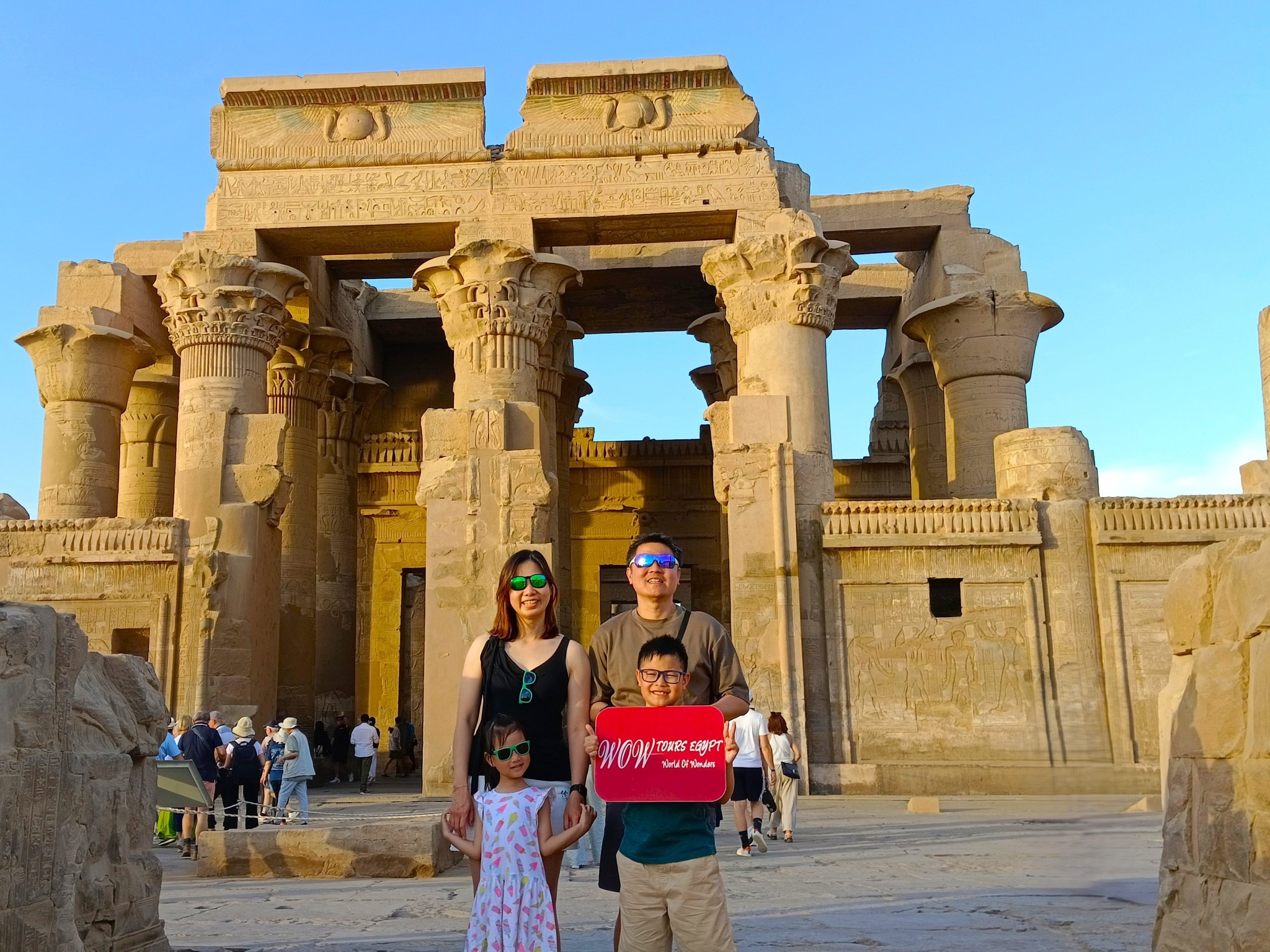 A happy family stands in front of the magnificent Temple of Kom Ombo in Upper Egypt, holding a WOW TOURS EGYPT // Luxor Front (9)