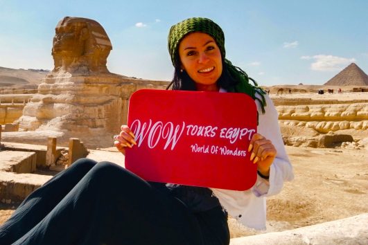 Woman holding WOW TOURS EGYPT sign near the Great Sphinx and a pyramid at the Giza Plateau in Cairo.
