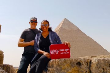 Couple holding a WOW TOURS EGYPT sign in front of the Pyramid of Khafre on the Giza Plateau in Cairo, Egypt.