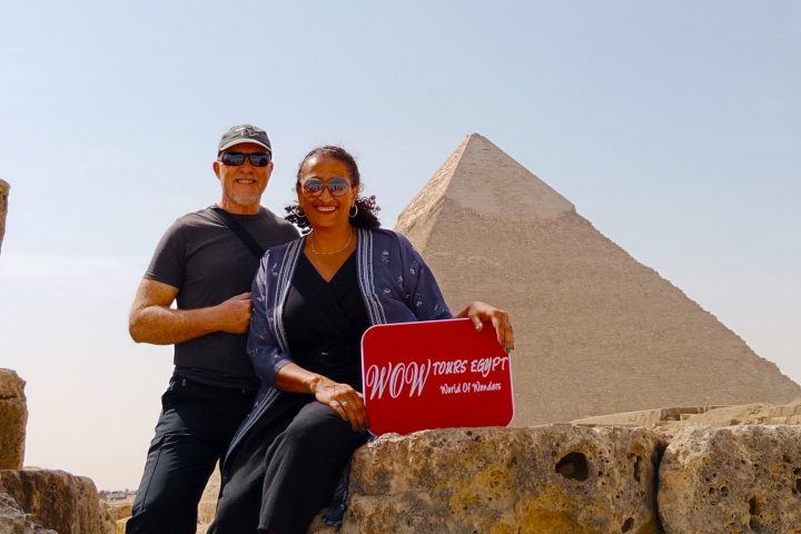 Couple holding a WOW TOURS EGYPT sign in front of the Pyramid of Khafre on the Giza Plateau in Cairo, Egypt.