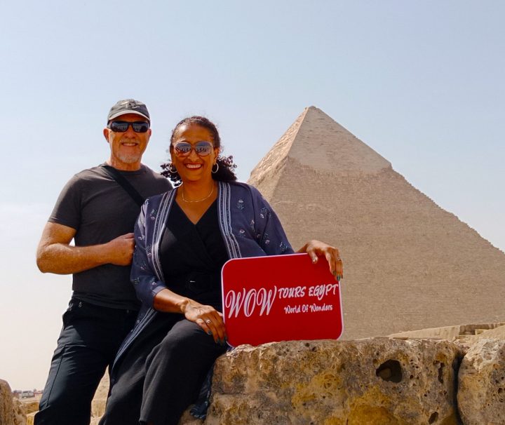 Couple holding a WOW TOURS EGYPT sign in front of the Pyramid of Khafre on the Giza Plateau in Cairo, Egypt.