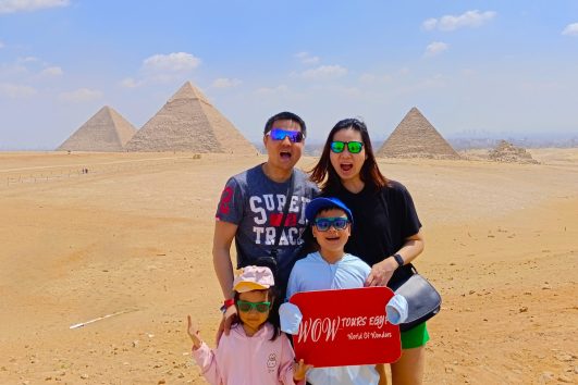 Family with two children holding a WOW TOURS EGYPT sign at the Great Pyramids of Giza in Cairo, Egypt.