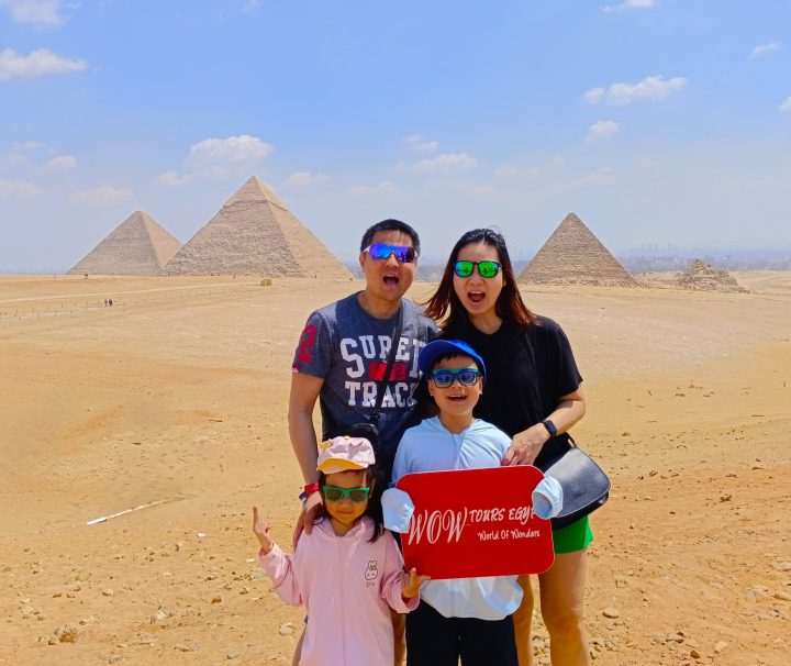 Family with two children holding a WOW TOURS EGYPT sign at the Great Pyramids of Giza in Cairo, Egypt.