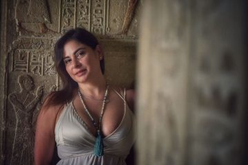 A woman stands inside the Temple of Hathor in Dendera, framed by ancient hieroglyphs and soft natural light.