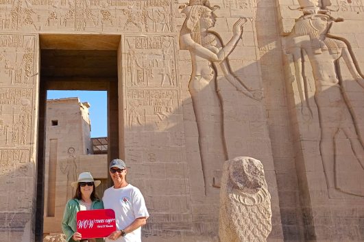 Couple standing at the entrance of Philae Temple in Aswan, holding a WOW Tours Egypt sign during a private guided tour. // Aswan front (9)