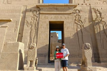 Couple standing at the entrance of Philae Temple in Aswan, holding a WOW Tours Egypt sign during a private guided tour.