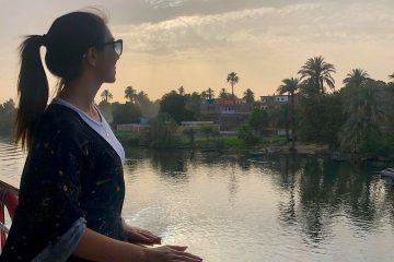 a lady standing on a Nile Cruise overlooking palm-lined banks and village life // Luxor front (7)