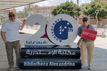 Smiling couple posing beside the 20th anniversary sign at Bibliotheca Alexandrina in Alexandria, Egypt.
