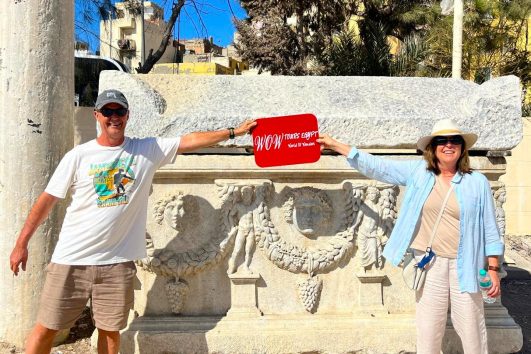 Visitors posing beside a decorated Greco-Roman sarcophagus at Kom El Shoqafa in Alexandria