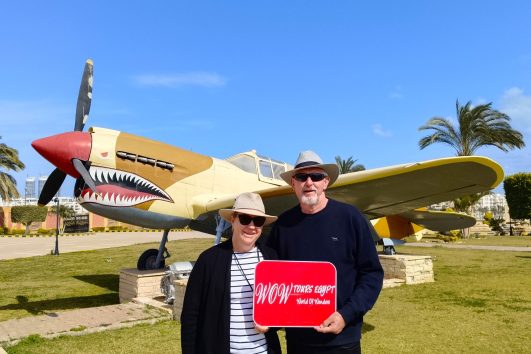 A couple posing beside a restored World War II aircraft in El Alamein, Egypt during a guided historical tour.