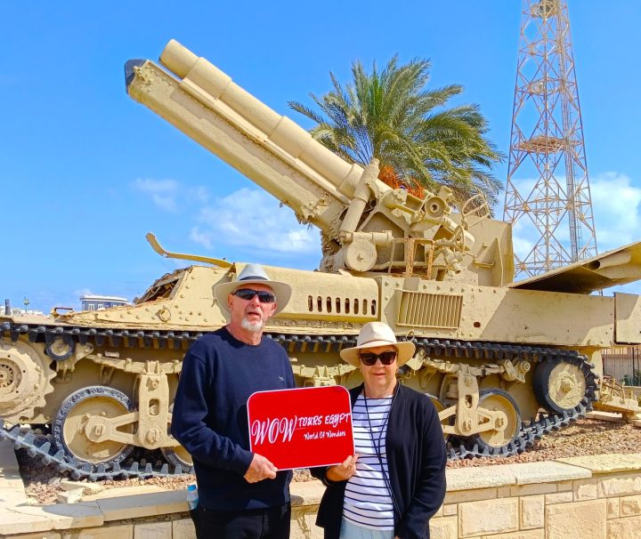 A couple standing beside a restored World War II artillery vehicle in El Alamein, Egypt during a historical guided tour.
