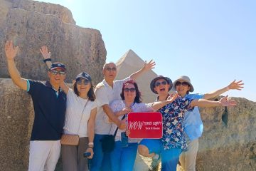 Excited group of travelers holding a WOW Tours Egypt sign in front of the Pyramid of Khafre in Cairo Egypt