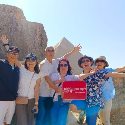 Excited group of travelers holding a WOW Tours Egypt sign in front of the Pyramid of Khafre in Cairo Egypt