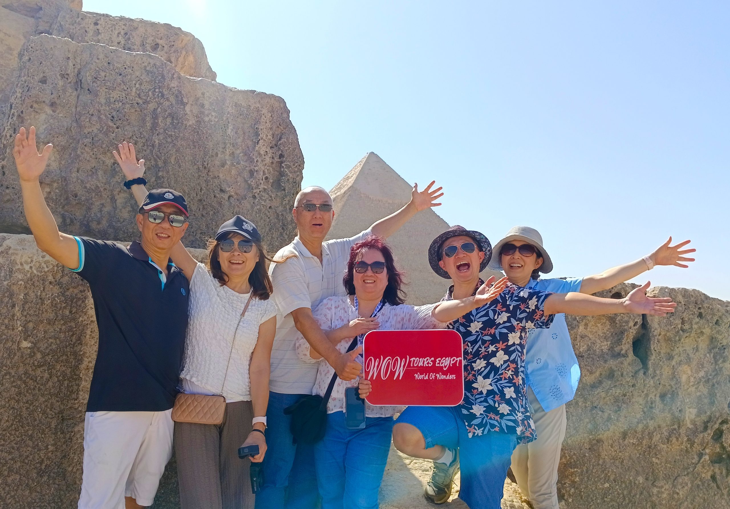 Excited group of travelers holding a WOW Tours Egypt sign in front of the Pyramid of Khafre in Cairo Egypt