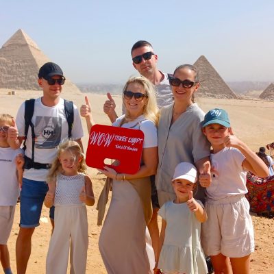 Happy family holding WOW Tours Egypt sign in front of the pyramids of Giza in Cairo Egypt