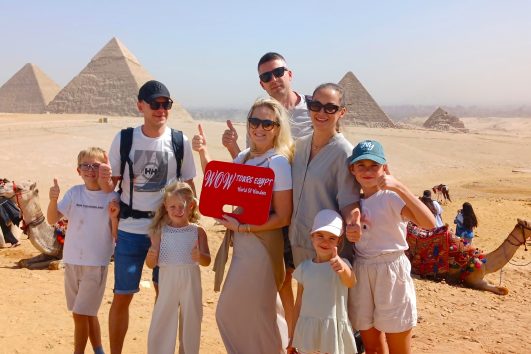 Happy family holding WOW Tours Egypt sign in front of the pyramids of Giza in Cairo Egypt