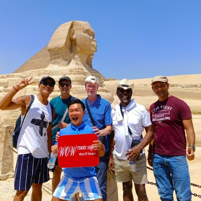 Travelers smiling and posing beside the Great Sphinx with the Great Pyramid of Khufu visible behind them in Giza