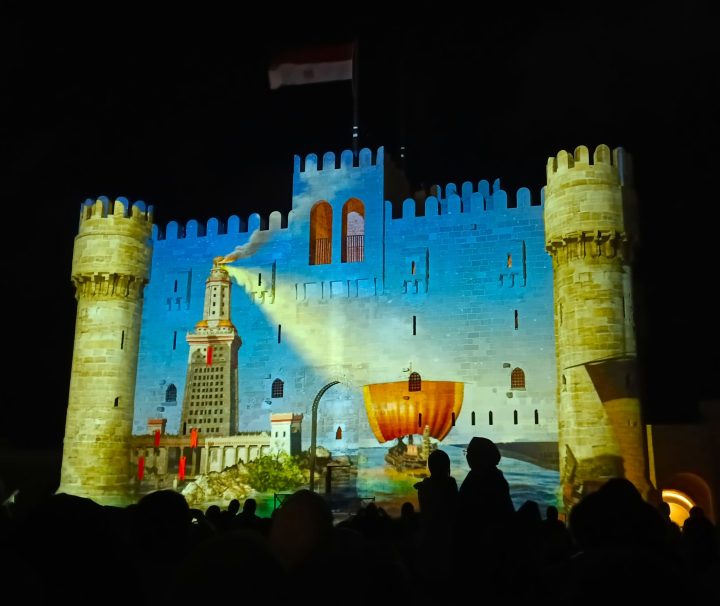 The Qaitbay Citadel in Alexandria, Egypt is illuminated during the Sound and Light Show, with projections of an ancient lighthouse and ship across its walls.